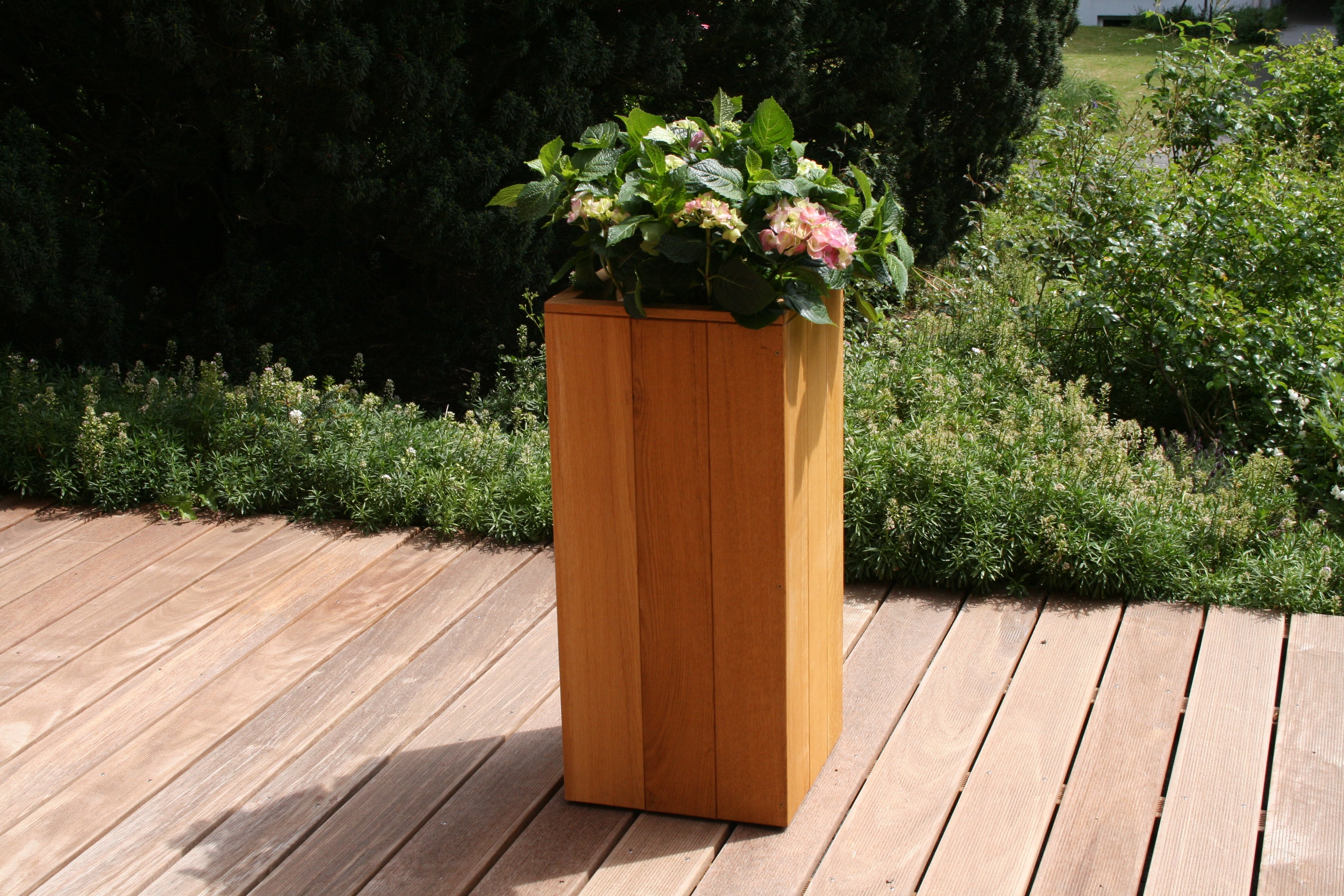 IPE-Terrassendiele 1-stg. geriffelt, 21 x 145 mm, als Bodenbelag im Außenbereich Holzterrasse aus IPE-Terrassendielen, 1-seitig geriffelt, 21 x 145 mm, im Außenbereich mit Blumenkübel aus Holz und grünem Pflanzbeet im Hintergrund