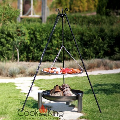 hug-grill-fruehling-500x500 Dreibeiniger Kochständer mit hängendem Grillrost, auf dem Würstchen und geschnittenes Gemüse liegen; darunter eine Feuerschale mit Holzscheiten, auf Rasen im Garten mit Hecke und Pflanzen im Hintergrund