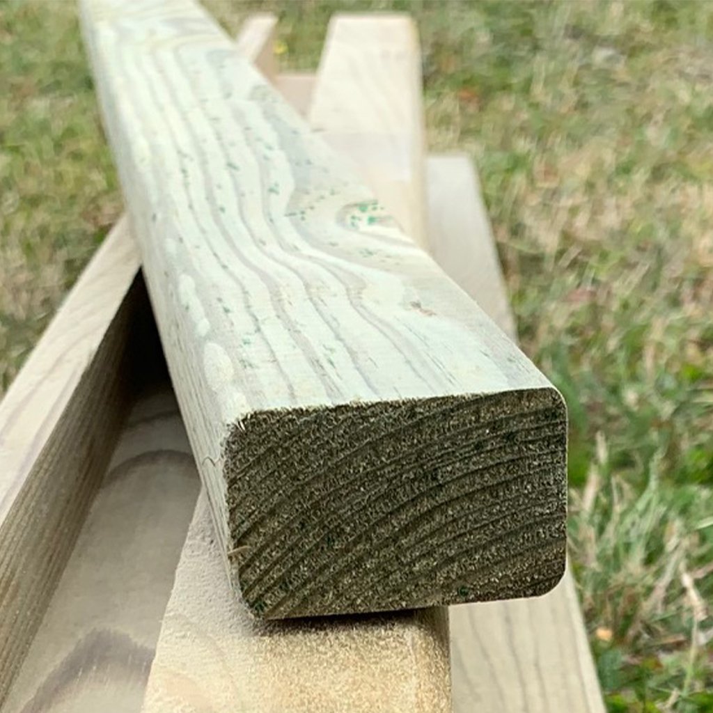 Nahaufnahme von hellen, unbearbeiteten Fichtenholzleisten für ein individuelles Hochbeet, mit sichtbarer Holzmaserung, gestapelt im Freien auf einer Wiese