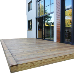Holz-Terrassendielen auf erhöhtem Podest vor modernem Haus mit großen Glasfronten, naturfarbene Dielen mit sichtbaren Fugen, sichtbare Terrassenkante und Fensterreflexionen von Bäumen