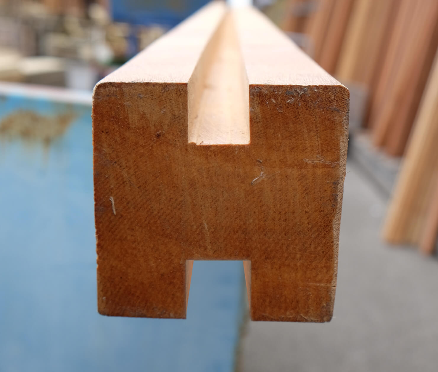 Nahaufnahme der Stirnseite eines Holzprofils mit einer Längsnut oben und einer rechteckigen Ausklinkung unten, raue Oberfläche, warmes Holz, unscharfer Werkstatt-Hintergrund