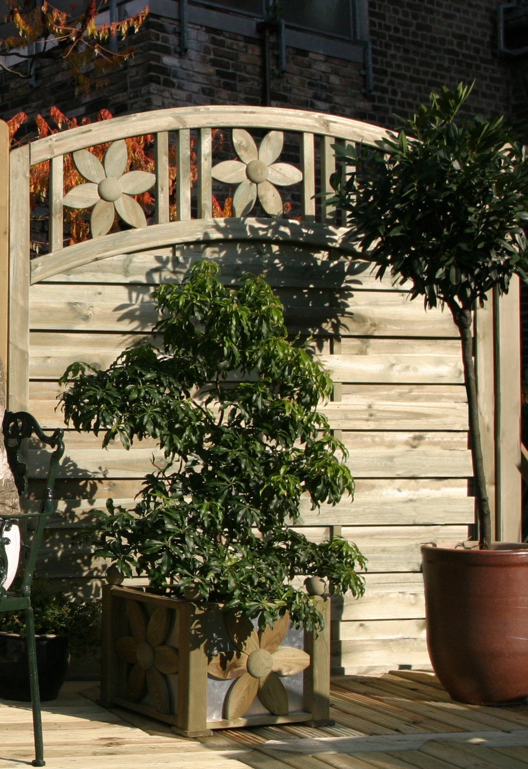Ornamentzaun Florenz mit Bogen aus kieferngrün imprägniertem Holz, oben mit Blumenornamenten, davor ein bepflanzter Blumenkasten mit ähnlichem Blumenmotiv und Topfpflanzen auf einer Terrasse im Garten