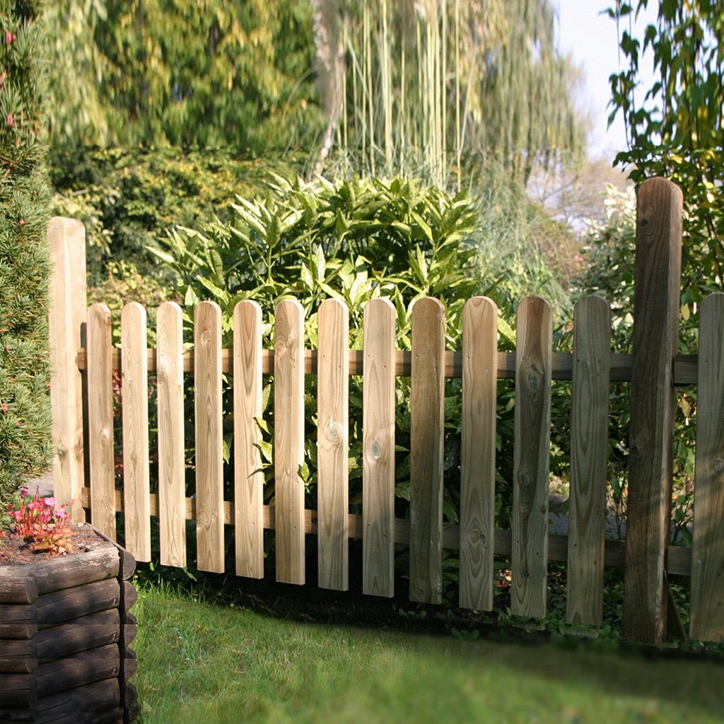 Holzzaun für den Vorgarten, Staketen kesseldruckimprägniert, Maße 18 x 90 mm und 22 x 70 mm Holz-Staketenzaun im Garten, kesseldruckimprägniert, mit senkrechten, abgerundeten Latten, vor dichten grünen Sträuchern und Pflanzen stehend, Produkt: Vorgartenzaun L.18 x 90 mm, R. 22 x 70 mm