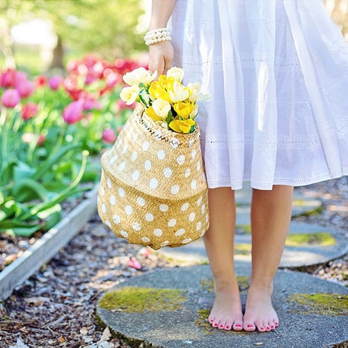 checkliste-garten-500x500 Barfüßige Frau im weißen Sommerkleid steht auf moosigem Steinweg, trägt Perlenarmband und hält gepunkteten Strohkorb voller gelber und weißer Tulpen, im Hintergrund blühende pinke Tulpen entlang eines Gartenwegs