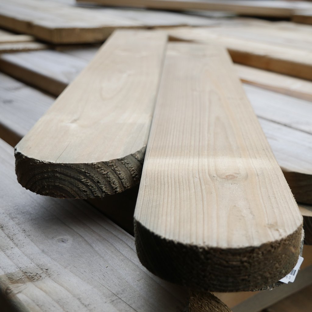 Zaunbrett Bamberg, glatt gehobelt, Maße 18 x 90 mm, kesseldruckimprägniert, mit abgerundetem Kopf; Nahaufnahme von zwei nebeneinanderliegenden Holzbrettern auf weiteren Holzbrettern.
