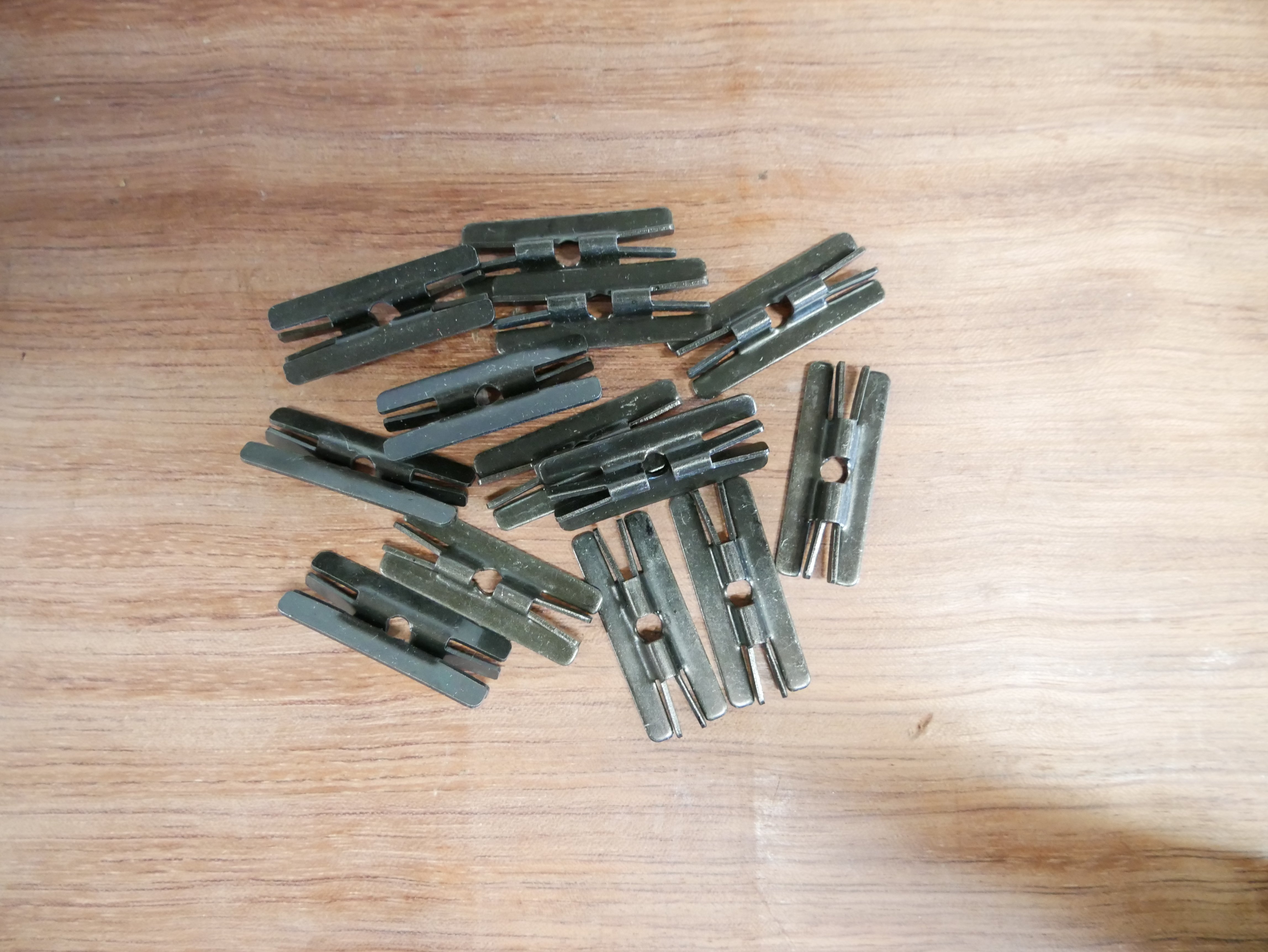 Metallclips für WPC/BPC Dielen, Paket mit 50 Stück, inklusive Schrauben Mehrere Metallclips für WPC/BPC Dielen auf einer Holzoberfläche, Produktfoto eines Pakets mit 50 Stück, Zubehör inkl. Schrauben für die Montage von Terrassendielen