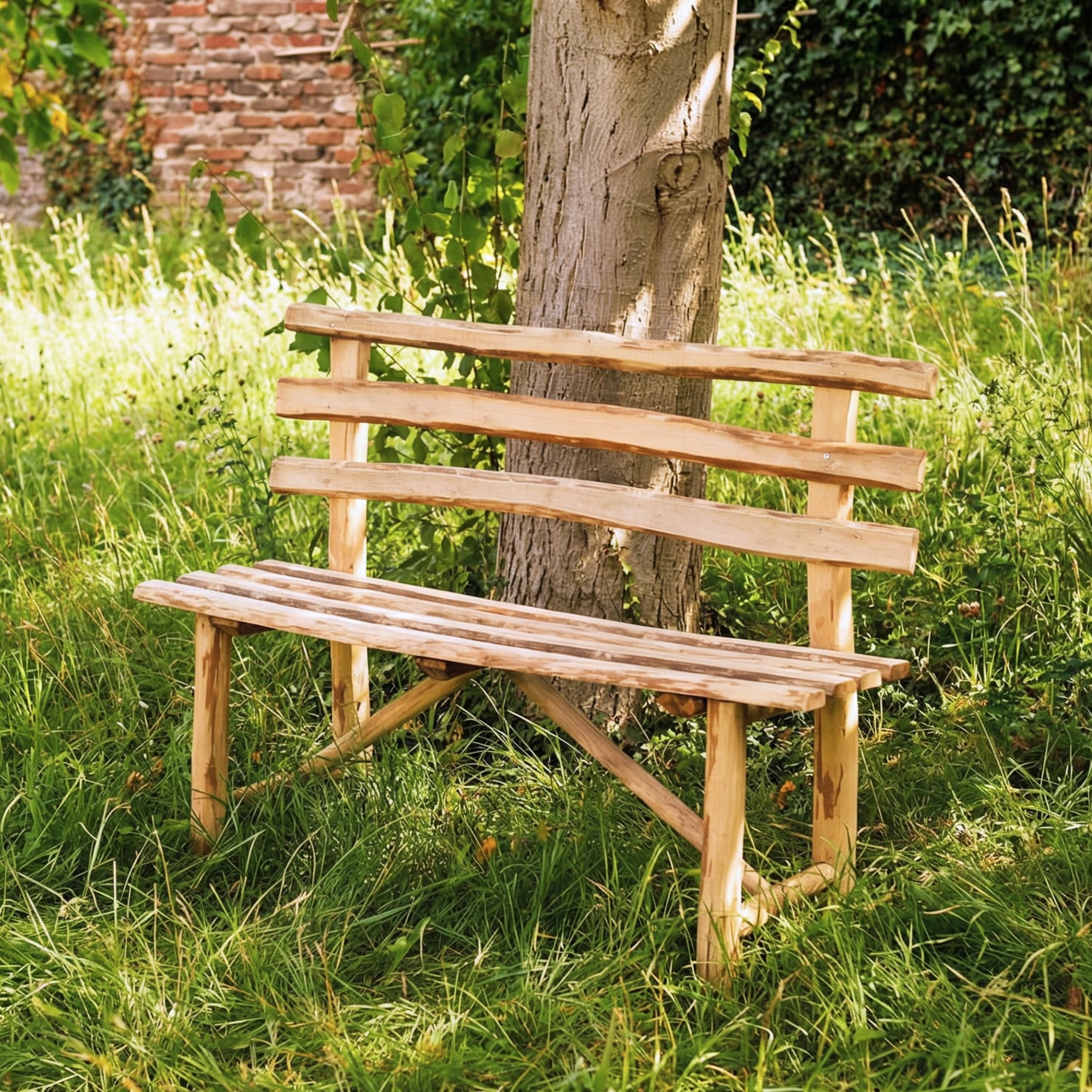 Rustique Bank aus Haselnuss, 118 cm Rustique Bank aus Haselnuss (118 cm), rustikale Holzbank mit geschwungenen, handgehobelten Latten und sichtbarer Maserung, helle natürliche Oberfläche, im hohen Gras vor einem Baum und einer alten Backsteinmauer im Garten