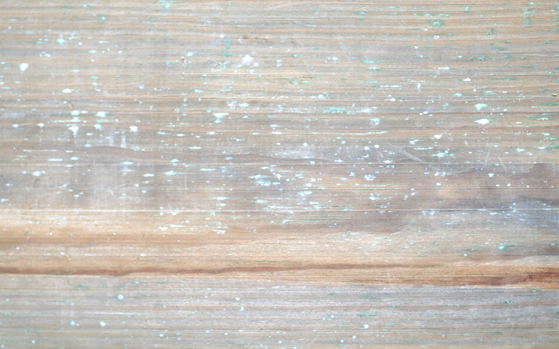 Nahaufnahme von hellbraunen, verwitterten Holzplanken mit feiner horizontaler Maserung, leichter Oberflächenabnutzung und verstreuten türkisen Farbflecken