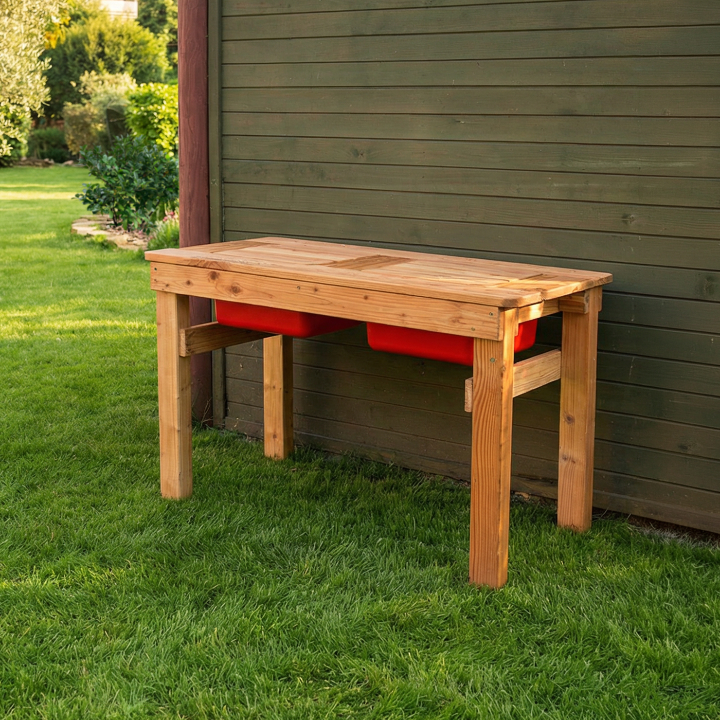 Spieltisch Wassermax aus Lärchenholz (100×50×60 cm) mit zwei roten Einsätzen, stehender Holztisch auf vier Beinen, platziert auf Rasen vor grün gestrichener Holzwand im Garten