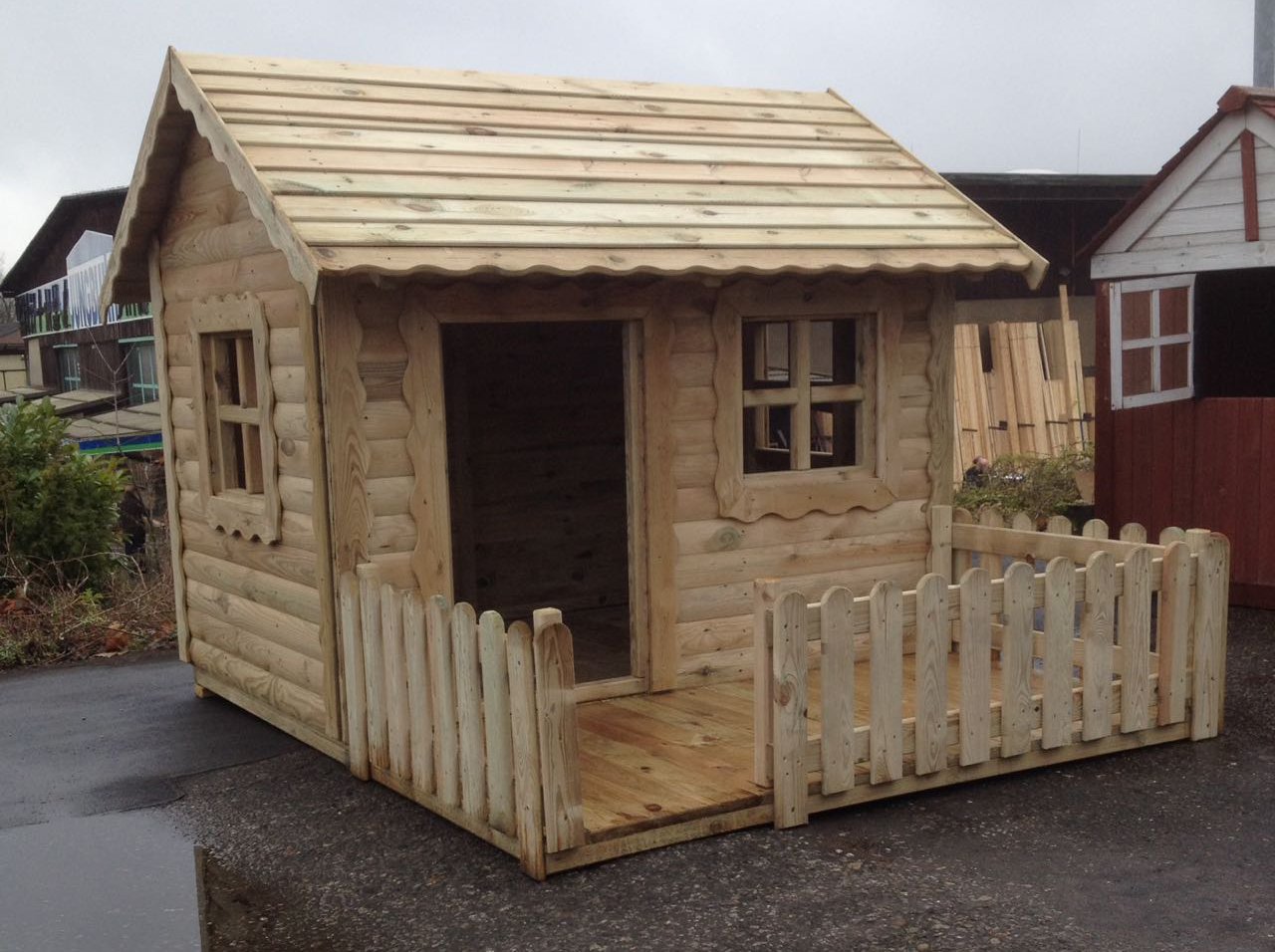 Kinderspielhaus Diana aus kesseldruckimprägniertem Holz, Maße 170 x 220 x 155 cm, mit Terrasse und Zaun Kinderspielhaus Diana aus hellem Holz, Maße 170 x 220 x 155 cm, kesseldruckimprägniert, mit Satteldach, zwei Fenstern, offenem Eingang und kleiner umlaufender Veranda mit Holzzaun, im Außenbereich aufgestellt