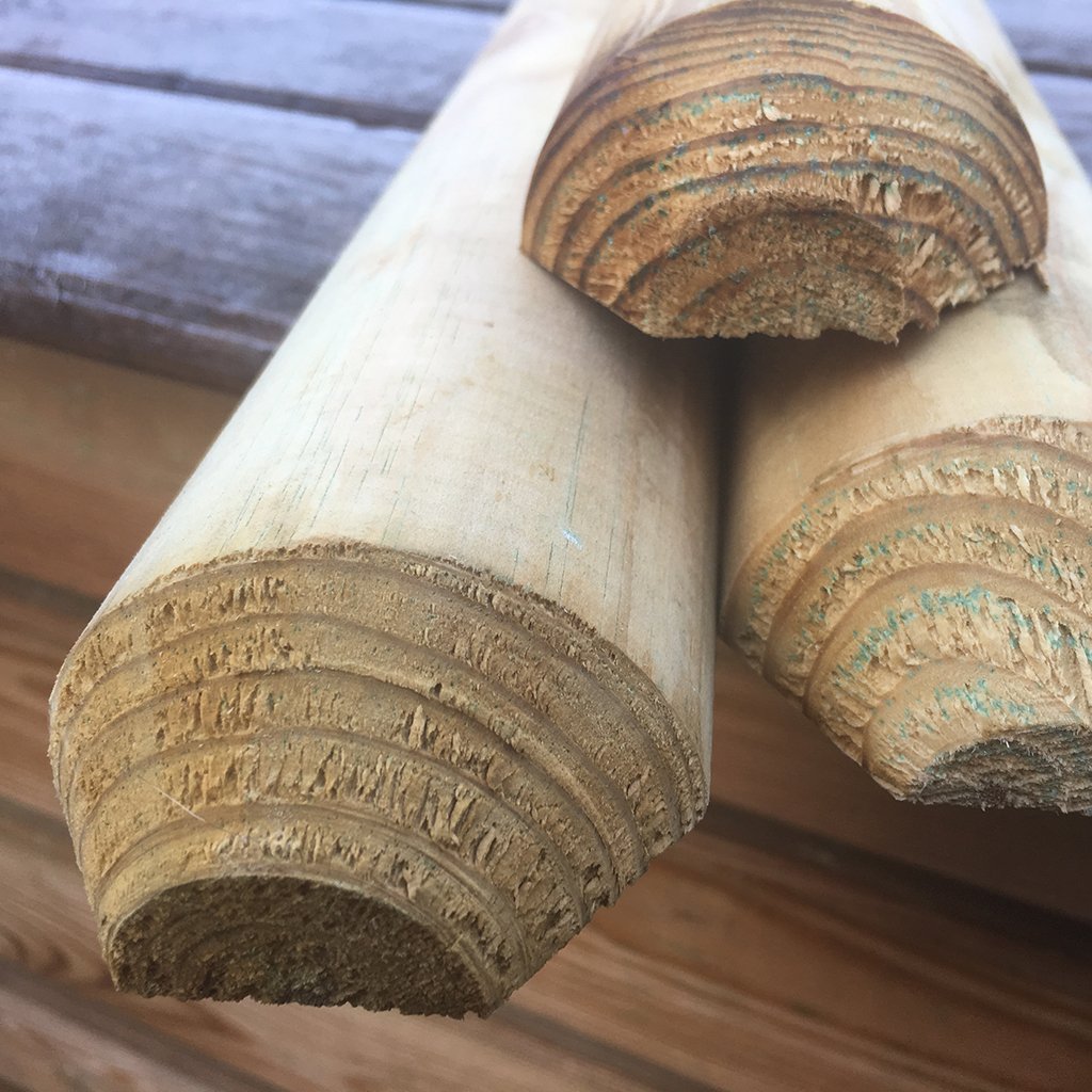 Nahaufnahme von drei gekegelten, kesseldruckimprägnierten Staketen aus naturbelassenem Holz, jeweils 6 cm stark, mit sichtbarer Maserung und Schnittkante, auf einer Holzoberfläche liegend